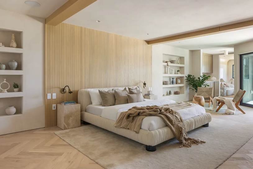 A bright, modern bohemian bedroom featuring a low-profile upholstered bed, light wood vertical paneling, built-in shelving, and neutral earth tones.