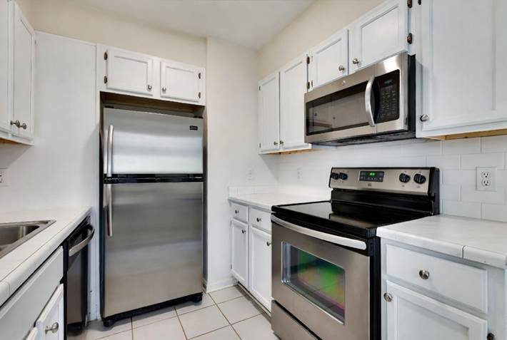 A bright kitchen with white cabinets, tile countertops, and stainless steel appliances. August Move-In Cleanings